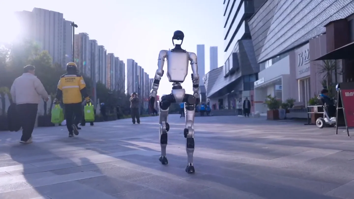 Robot humanoïde Unitree G1 marchant au milieu d’une rue piétonne d’une grande ville chinoise, passants de dos et tours d’habitation au loin