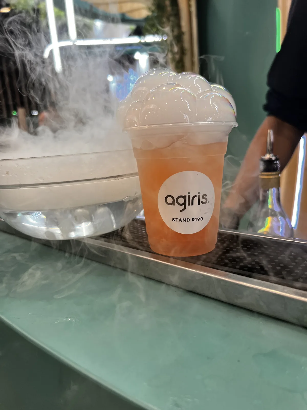 Un cocktail dans un gobelet au logo AGIRIS, stand R190, sur le bar des Potions du Cabinet, dans un nuage de fumée