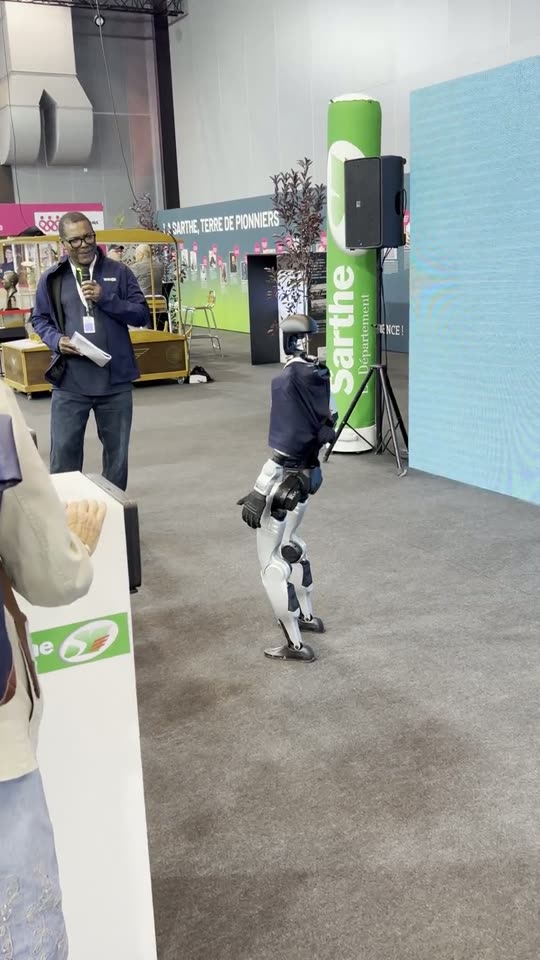 Le robot en polo Jolivet dans les allées d'un hall de la foire, les visiteurs de dos