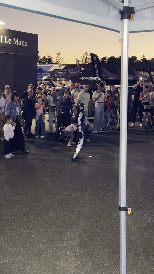 Le stand Jolivet à la tombée de la nuit, les visiteurs rassemblés autour du robot