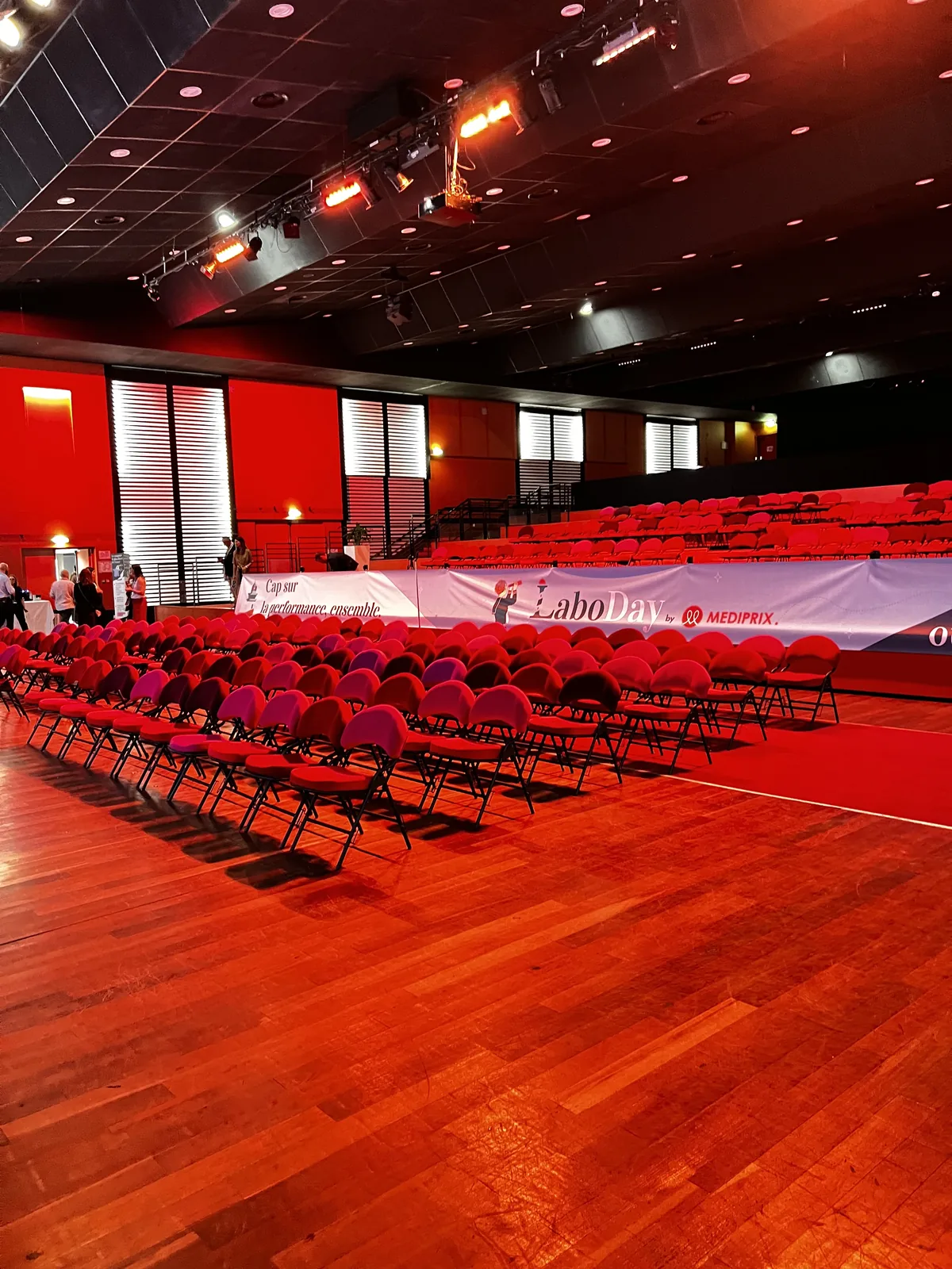 La salle plénière du Pasino, chaises rouges en rangs, une banderole Labo Day et Médiprix au fond