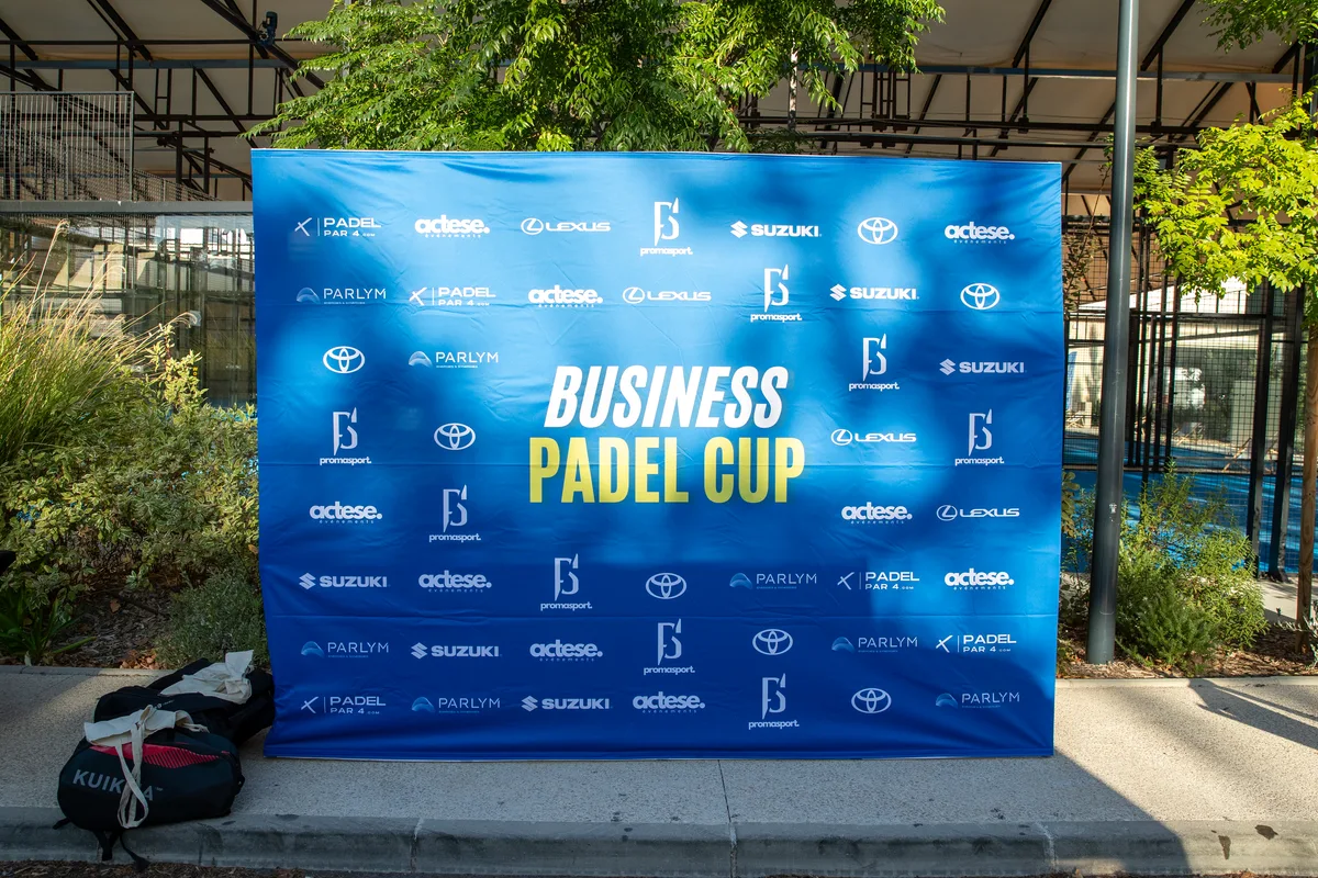 Le mur de la Business Padel Cup, logos d'Actese Événements, de Promasport et des partenaires du tournoi, au bord d'une allée du Set Club