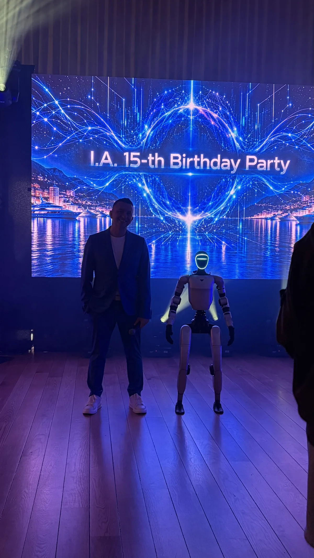 L'animateur de la soirée et le robot humanoïde côte à côte devant l'écran géant de la fête
