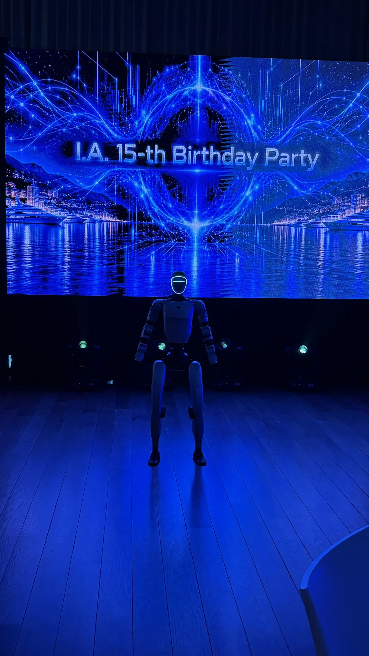 Le robot humanoïde, visière allumée, debout seul sur la piste au pied de l'écran géant « I.A. 15-th Birthday Party »