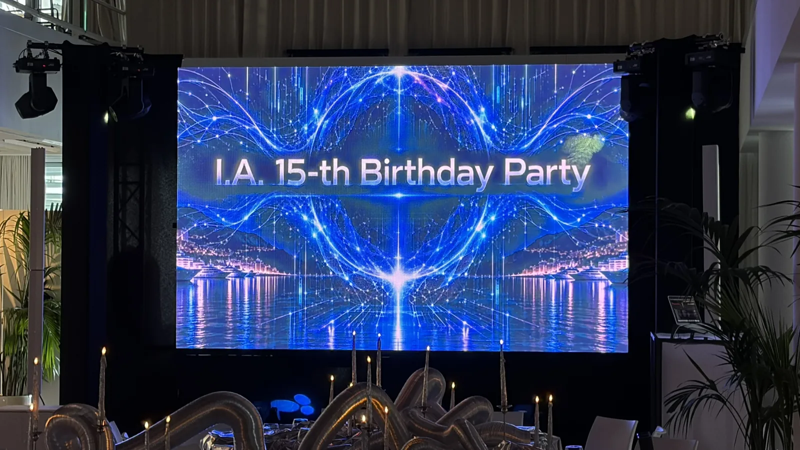 La salle Ballroom avant l'arrivée des invités : l'écran géant « I.A. 15-th Birthday Party », les projecteurs et les tables décorées de ballons argentés