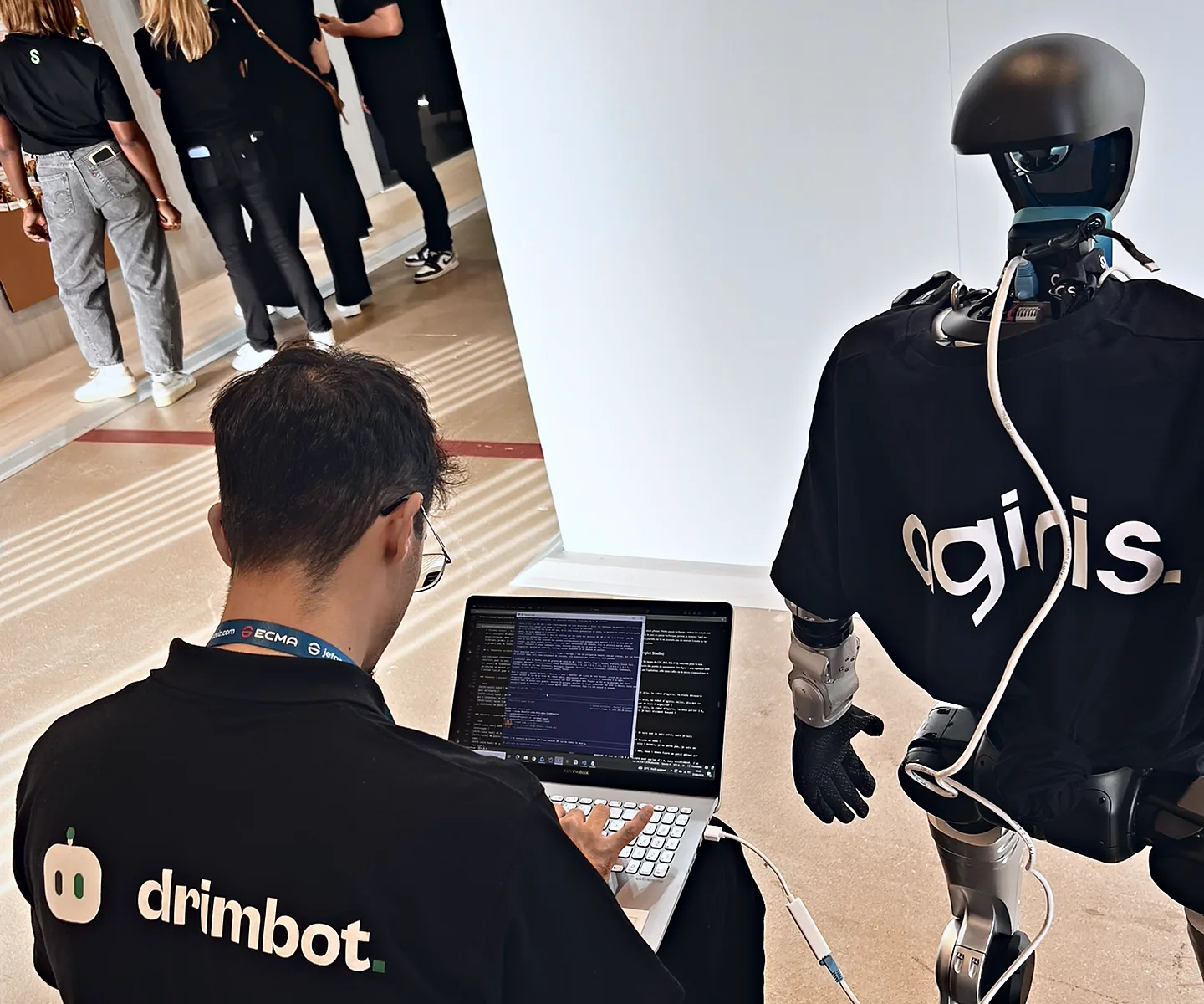 Ibrahim, fondateur de Drimbot, programme sur son ordinateur portable le robot humanoïde Unitree G1 EDU habillé aux couleurs d'Agiris, relié par un câble Ethernet, sur le stand Agiris